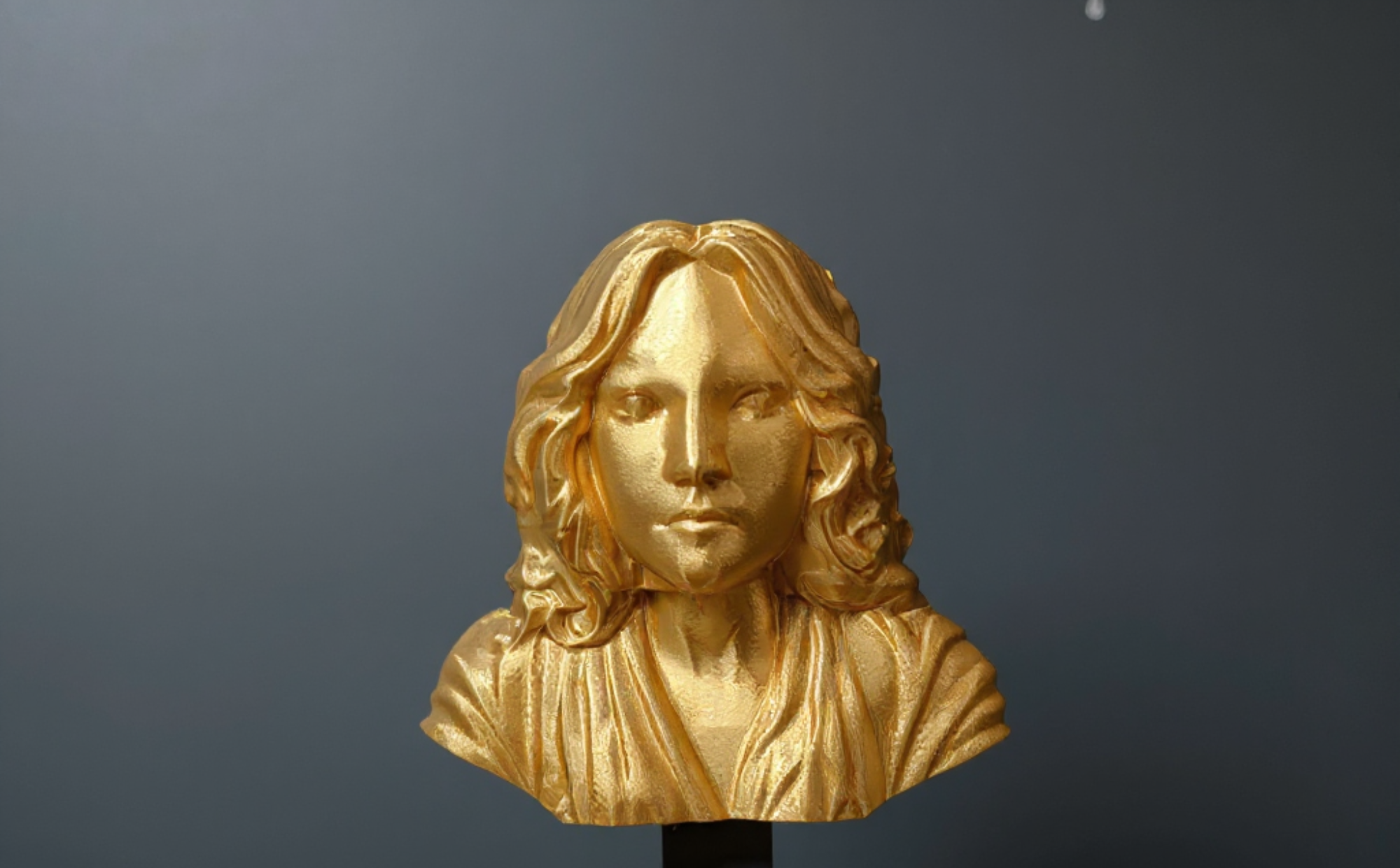 Finished gold portrait sculpture against a dark background