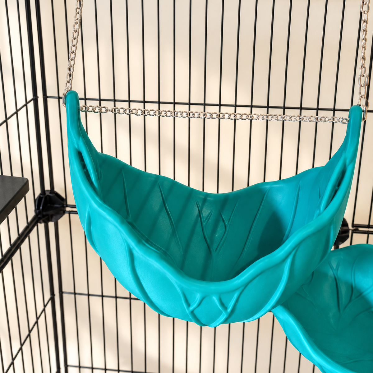 High-angle view into the empty teal-green leaf hammock, showing its interior and hanging chain.