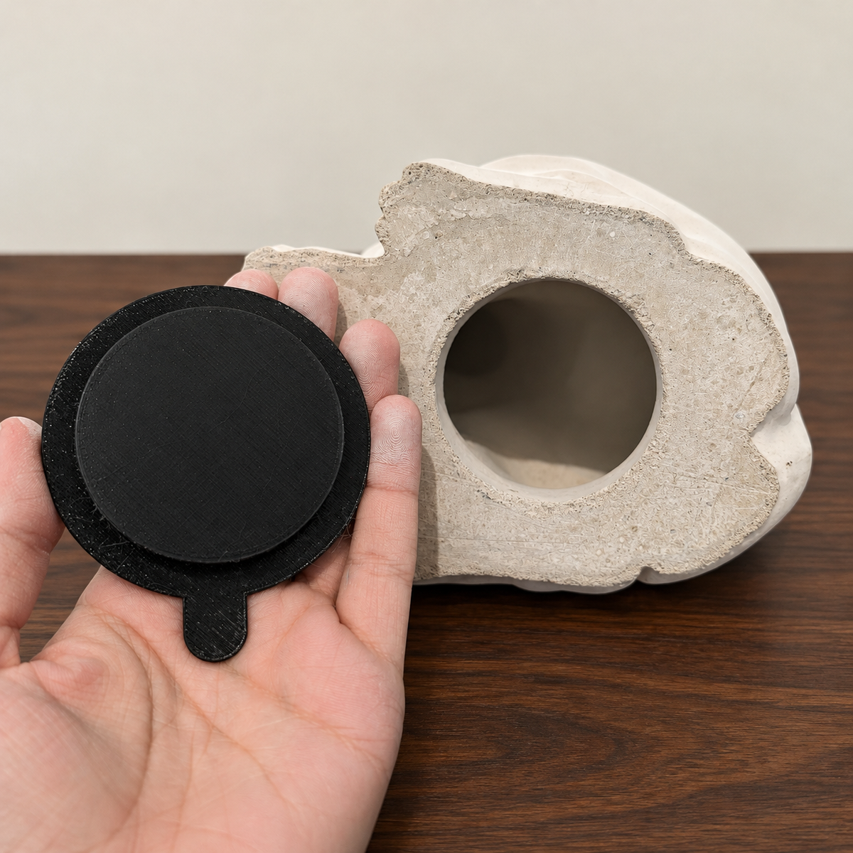 Hand holding a fully black plug beside the opening of a non-jar urn