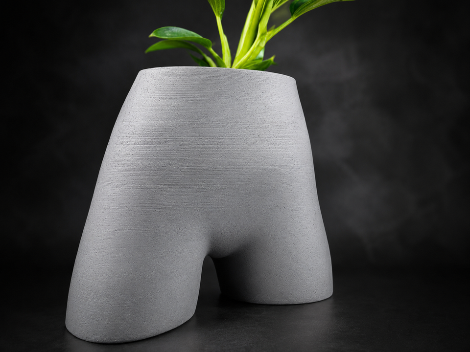 Side view of Cheeky Bum cast stone planter with plant on dark backdrop