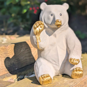 White cast stone honey bear garden ornament with raised gold paw and gold feet outdoors