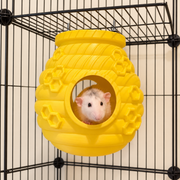 Pale rat looking forward from the round entrance of a yellow beehive hide mounted beneath cage-roof bars.