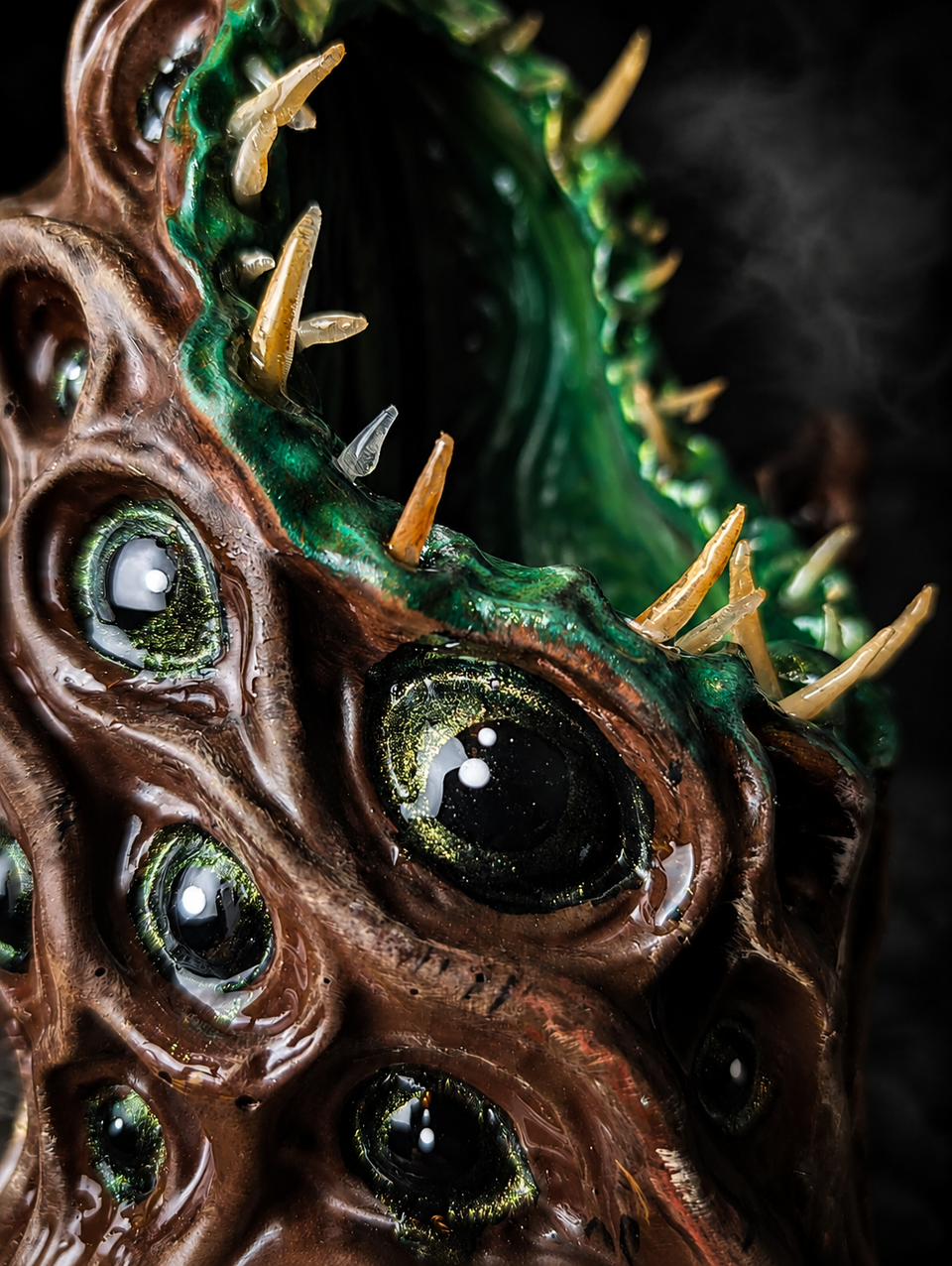 Close detail of The Watching Maw glossy black-and-gold eyes and pale teeth