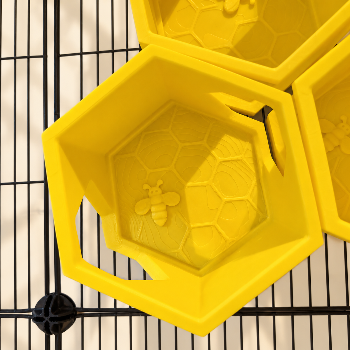 Close view of the bee relief and honeycomb pattern inside a yellow shelf, with side openings and partial neighbouring shelves.