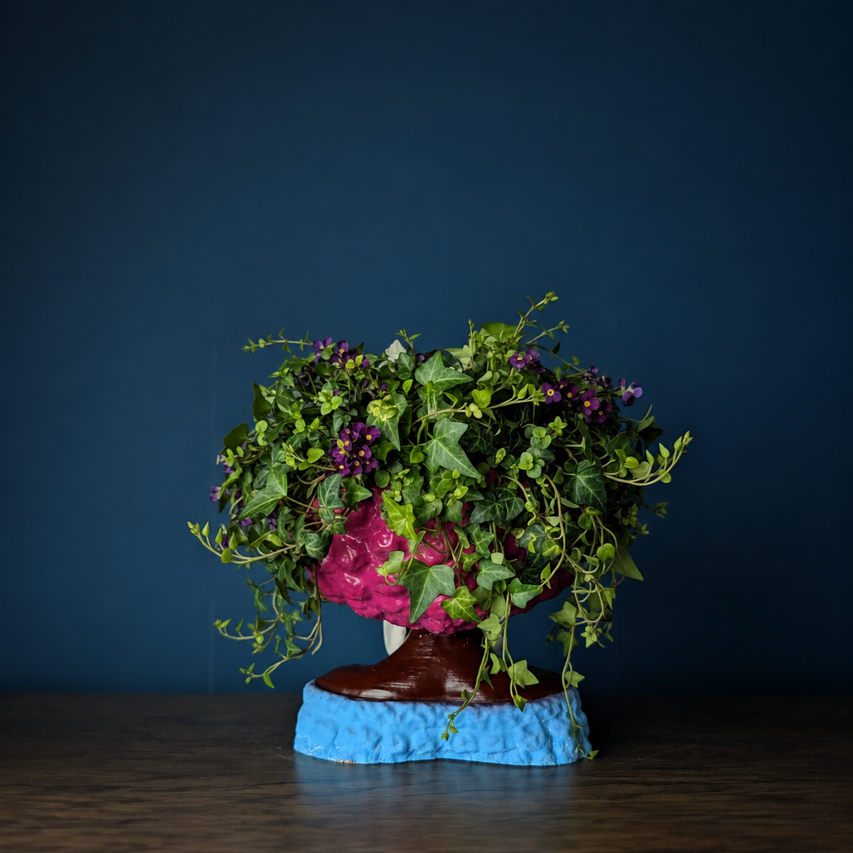 Girl Juice head planter filled with trailing greenery against a deep blue wall