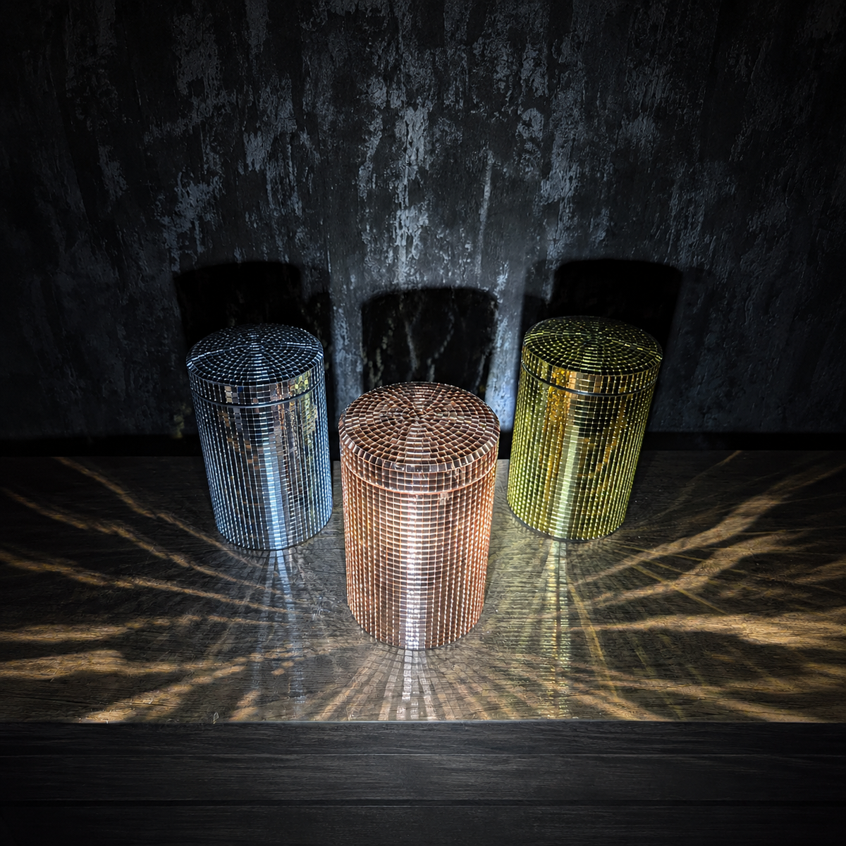 Silver, rose gold and gold mirror canisters reflecting light in a dark setting