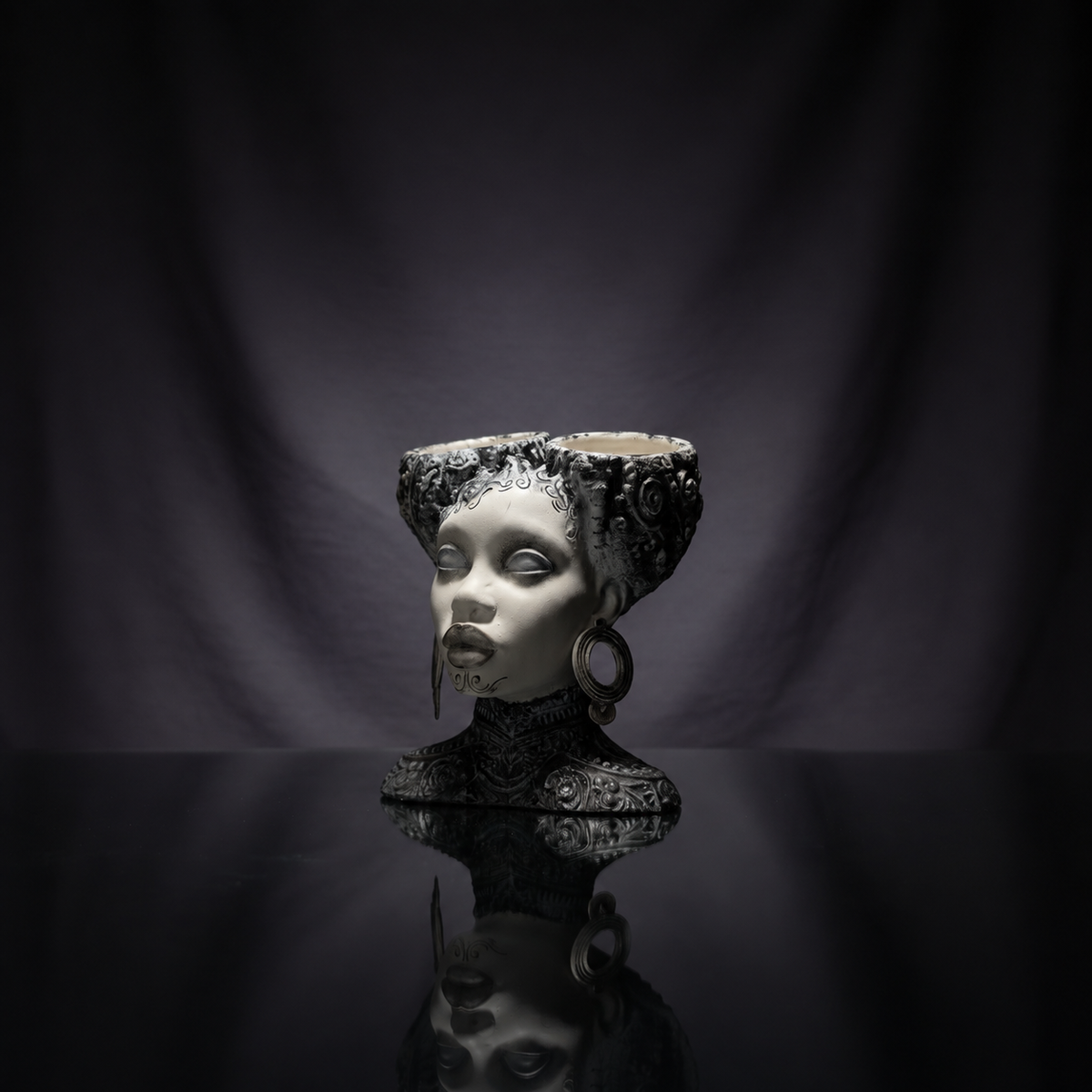 Gothic twin bowl head planter on a black reflective surface with draped fabric