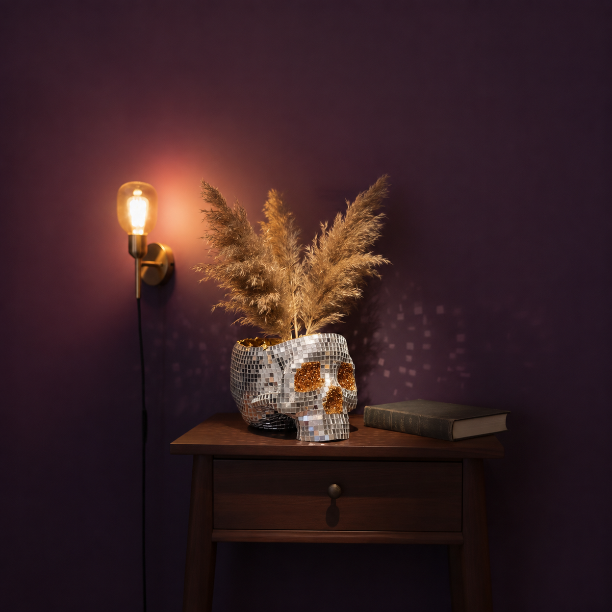 Disco skull planter with pampas grass on a dark bedside table beside a wall lamp and closed book