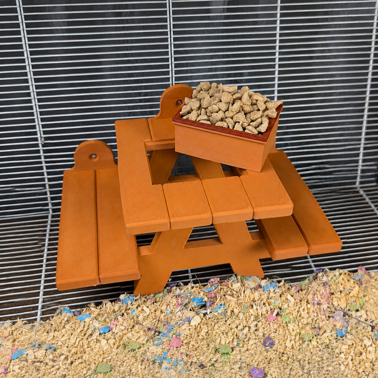 Orange rat picnic bench with filled food bowl attached inside a cage